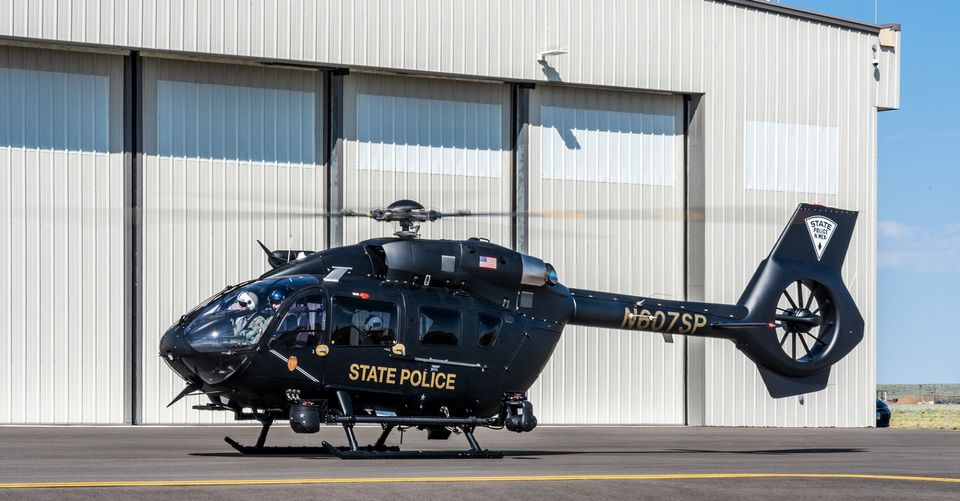 Black helicopter marked State Police parked outside a large gray hanger