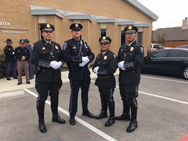 Four uniformed officers with hands crossed stand outside yellow brick building